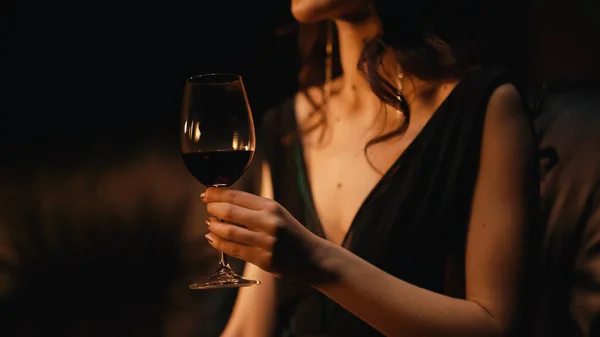 Vista recortada de la elegante mujer joven sosteniendo vaso de vino y sentado en el sofá en negro - foto de stock