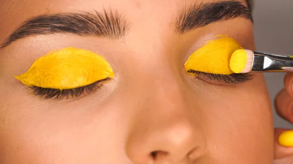 Обрезанный вид женщины, использующей желтую кремовую тень для век с помощью косметической щетки — Stock Photo