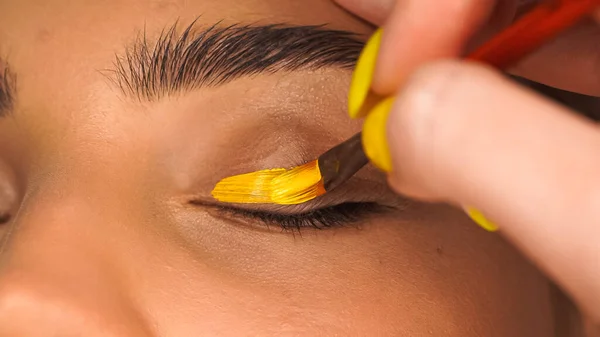 Close up view of woman applying yellow creamy eye shadow with cosmetic brush — Stock Photo