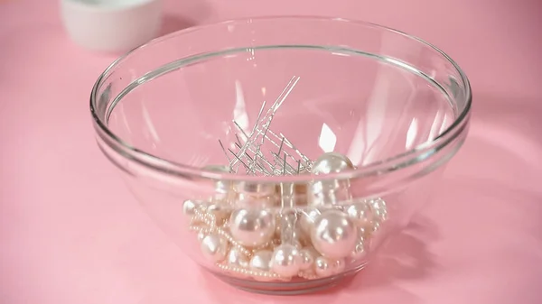 Alfinetes de cabelo com pérolas em tigela de vidro em rosa — Fotografia de Stock