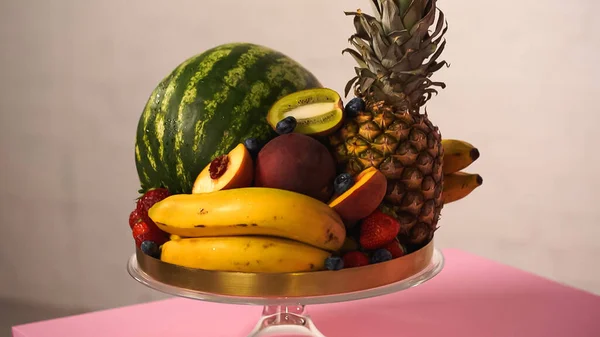 Vari di deliziosi frutti e bacche su stand torta rosa — Foto stock