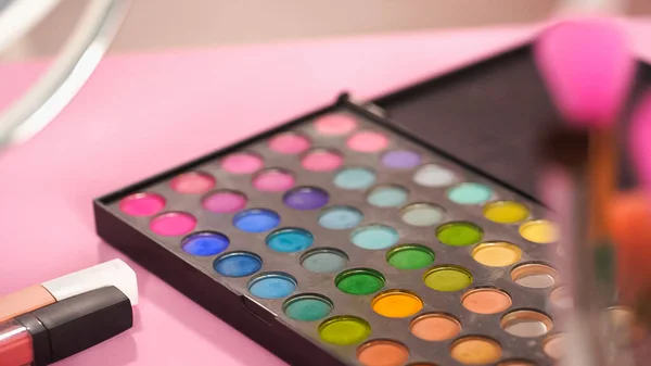 Eye shadow palette and different colors on pink — Stock Photo