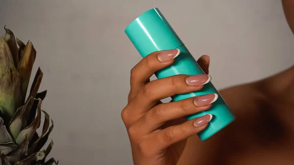Partial view of woman shaking blue bottle on grey — Stock Photo