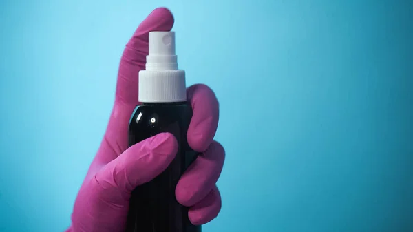 Cropped view of person in rubber glove holding spray bottle on blue — Stock Photo