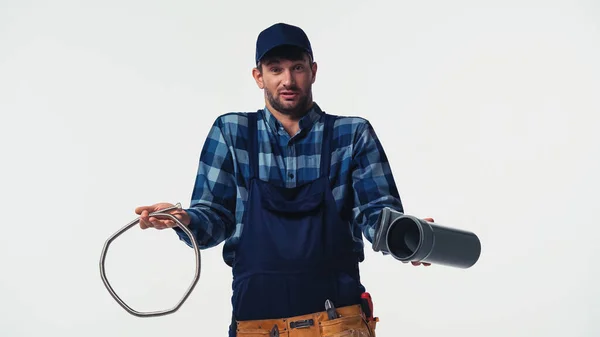 Confused plumber holding pipes and looking at camera isolated on white — Stock Photo