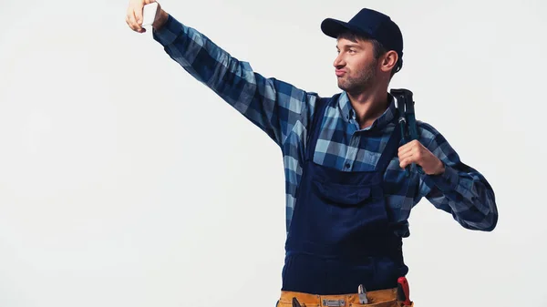 Arbeiter schmollt Lippen, während er einen Rohrschlüssel in der Hand hält und ein Selfie auf weißem Grund macht — Stockfoto