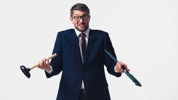 Confused businessman in formal wear holding pipe wrench and plunger isolated on white — Stock Photo