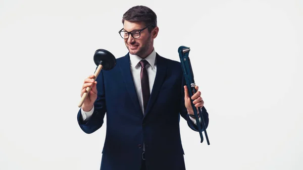 Hombre de negocios positivo en traje y gafas que sostienen el émbolo y la llave inglesa aislados en blanco - foto de stock