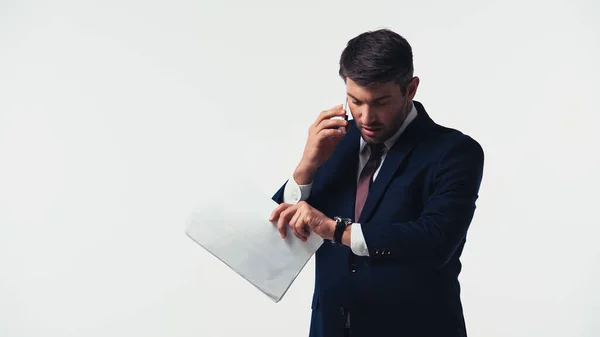 Hombre de negocios hablando en el teléfono inteligente mientras sostiene los papeles y mirando reloj de pulsera aislado en blanco - foto de stock