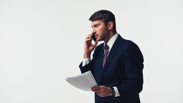 Vista lateral del hombre de negocios con papeles hablando en el teléfono celular aislado en blanco - foto de stock