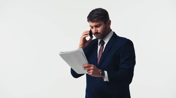 Uomo d'affari arrabbiato guardando i documenti mentre parla su smartphone isolato su bianco — Foto stock