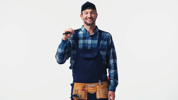 Lächelnder Arbeiter in Uniform, der einen Rohrschlüssel in der Hand hält und isoliert auf weiß in die Kamera blickt — Stockfoto