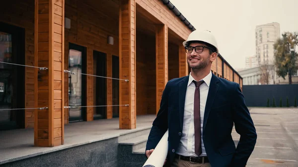 Happy engineer in white hardhat holding blueprint on urban street — Stock Photo