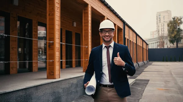 Engenheiro sorridente com planta mostrando como perto de construção ao ar livre — Fotografia de Stock