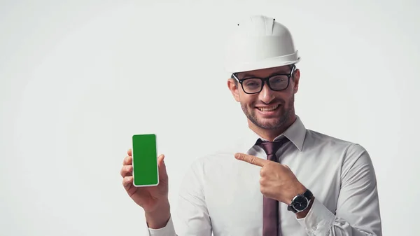 Arquitecto en casco apuntando al teléfono celular con pantalla verde aislada en blanco - foto de stock