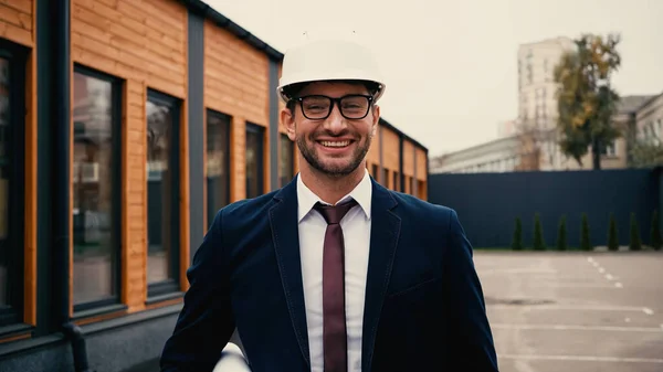 Architect in eyeglasses and helmet holding blueprint on urban street — Stock Photo