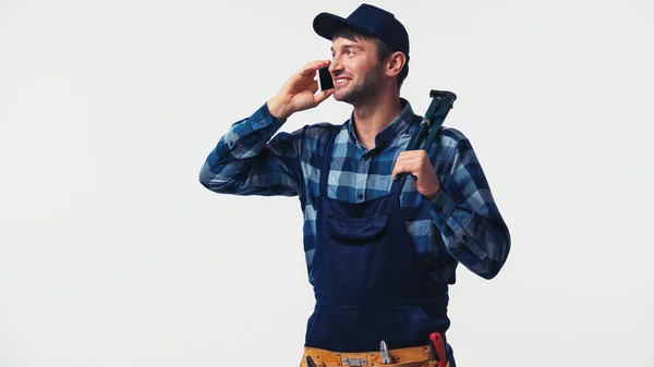 Trabajador positivo con llave de tubo hablando en smartphone aislado en blanco - foto de stock