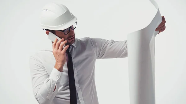 Architect in hardhat talking on smartphone and looking at blueprint isolated on white — Stock Photo