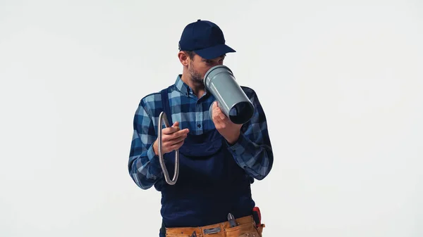 Handyman em macacão olhando para tubo de plástico isolado em branco — Fotografia de Stock