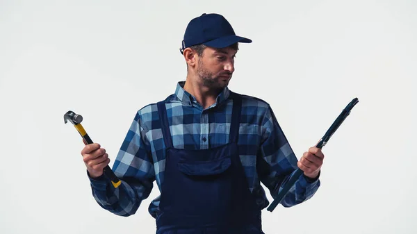 Serviceman in overalls holding pipe wrench and hammer isolated on white — Stock Photo