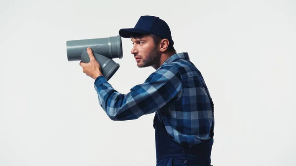 Side view of plumber looking through plastic pipe isolated on white — Stock Photo