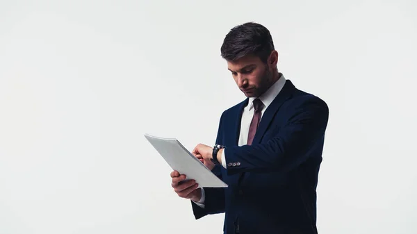 Hombre de negocios mirando el reloj de pulsera mientras sostiene papeles aislados en blanco - foto de stock