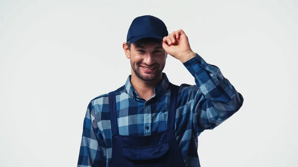 Happy workman adjusting cap and looking at camera isolated on white — Stock Photo