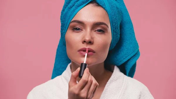 Jeune femme avec serviette bleue sur la tête appliquant brillant à lèvres isolé sur rose — Photo de stock