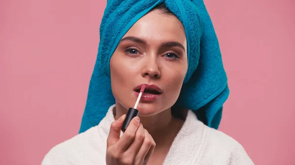 Pretty woman applying lip gloss while looking at camera isolated on pink — Stock Photo