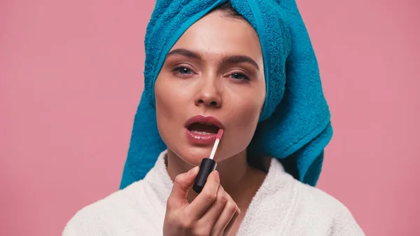 Mulher com toalha terry na cabeça aplicando gloss labial isolado em rosa — Fotografia de Stock