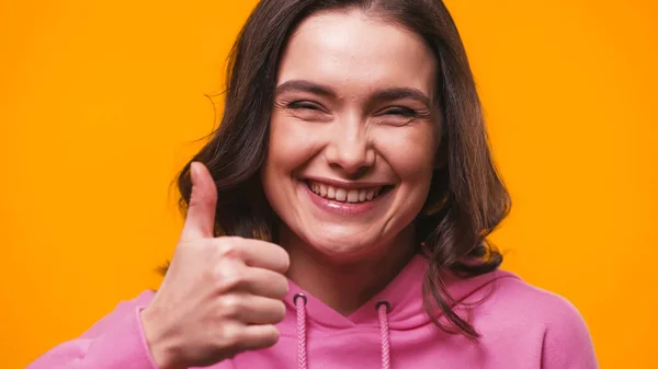 Excited woman showing thumb up while looking at camera isolated on yellow — Stock Photo