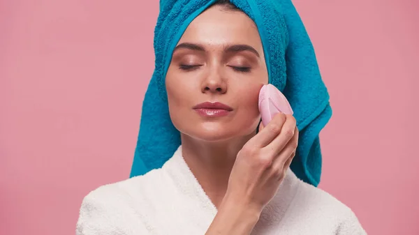 Mujer joven con los ojos cerrados utilizando limpiador facial de silicona aislado en rosa - foto de stock