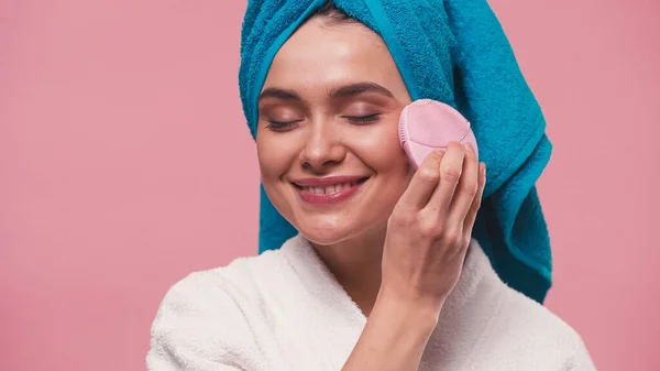 Donna gioiosa utilizzando detergente viso in silicone con gli occhi chiusi isolati su rosa — Foto stock