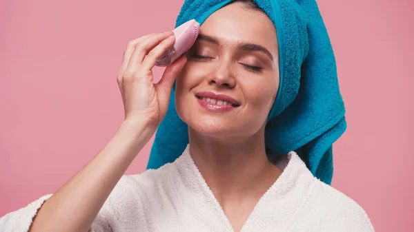 Happy woman using silicone facial cleanser with closed eyes isolated on pink — Stock Photo
