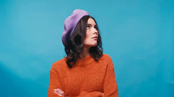 Offensée femme au béret lilas debout avec les bras croisés et regardant loin isolé sur bleu — Photo de stock