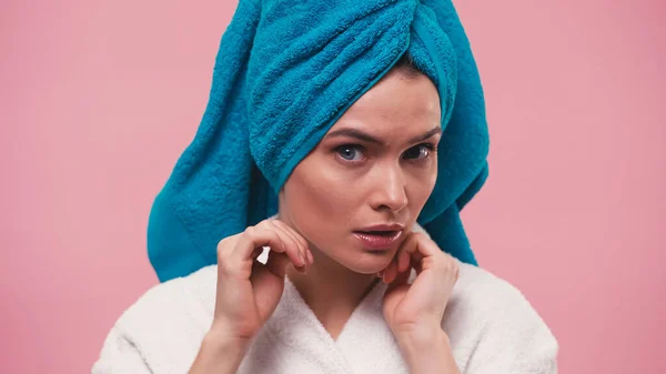 Femme réfléchie avec serviette bleue sur la tête en regardant la caméra isolée sur rose — Photo de stock