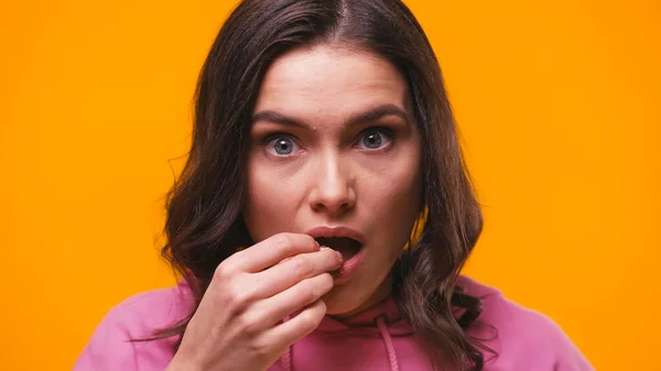 Shocked woman eating popcorn while watching breathtaking film isolated on yellow — Stock Photo