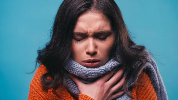 Mujer enferma en bufanda de punto tos con los ojos cerrados aislados en azul - foto de stock