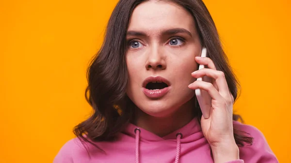 Mujer conmocionada con la boca abierta llamando en el teléfono inteligente aislado en amarillo — Stock Photo