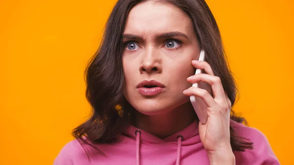 Wütende Frau in rosa Kapuzenpulli spricht auf Smartphone isoliert auf gelb — Stockfoto