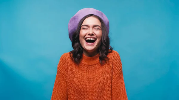 Excited woman in beret and jumper laughing with closed eyes isolated on blue — Stock Photo