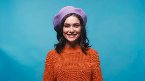 Femme joyeuse en pull orange et béret violet regardant la caméra isolée sur bleu — Photo de stock