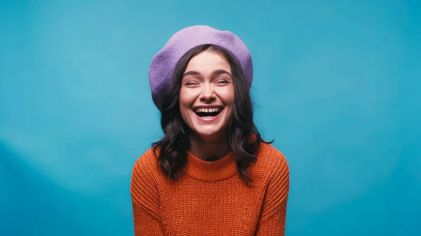 Excited woman in warm sweater and beret laughing isolated on blue — Stock Photo