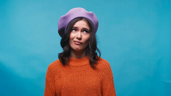 Verwirrte Frau in fliederfarbener Baskenmütze schaut vereinzelt auf blauem Grund weg — Stockfoto