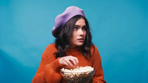 Frightened woman with bowl of popcorn watching movie isolated on blue — Stock Photo