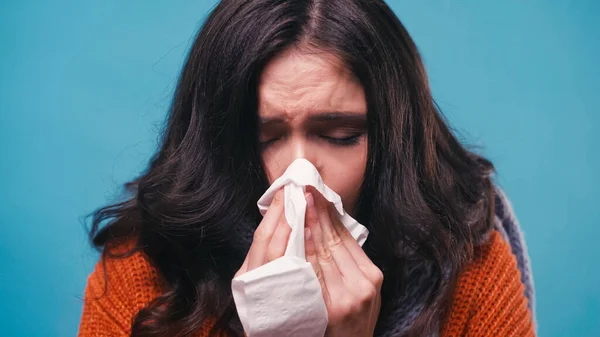 Sick woman with closed eyes sneezing in paper napkin isolated on blue — Stock Photo