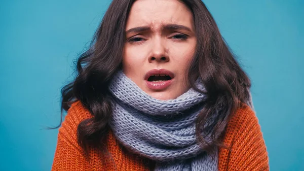 Ill woman in knitted scarf sneezing while looking at camera isolated on blue — Stock Photo