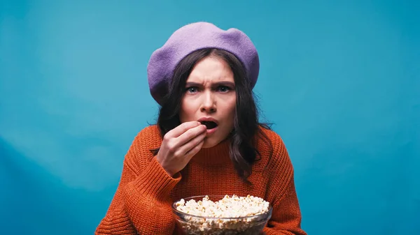 Nervöse Frau isst Popcorn, während sie aufregenden Film isoliert auf blau sieht — Stockfoto