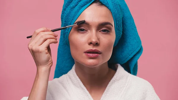 Mulher com toalha na cabeça styling sobrancelhas com escova de sobrancelha isolada em rosa — Fotografia de Stock