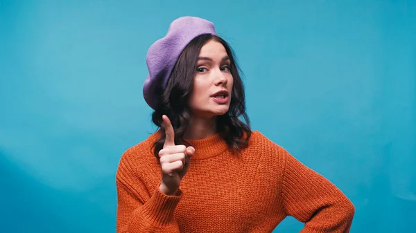 Strict woman in beret talking at pointing with finger isolated on blue — Stock Photo